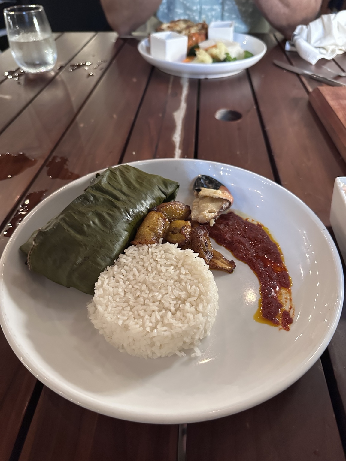 Banana-leaf parcel with white rice, fried plantains, fish and red sauce