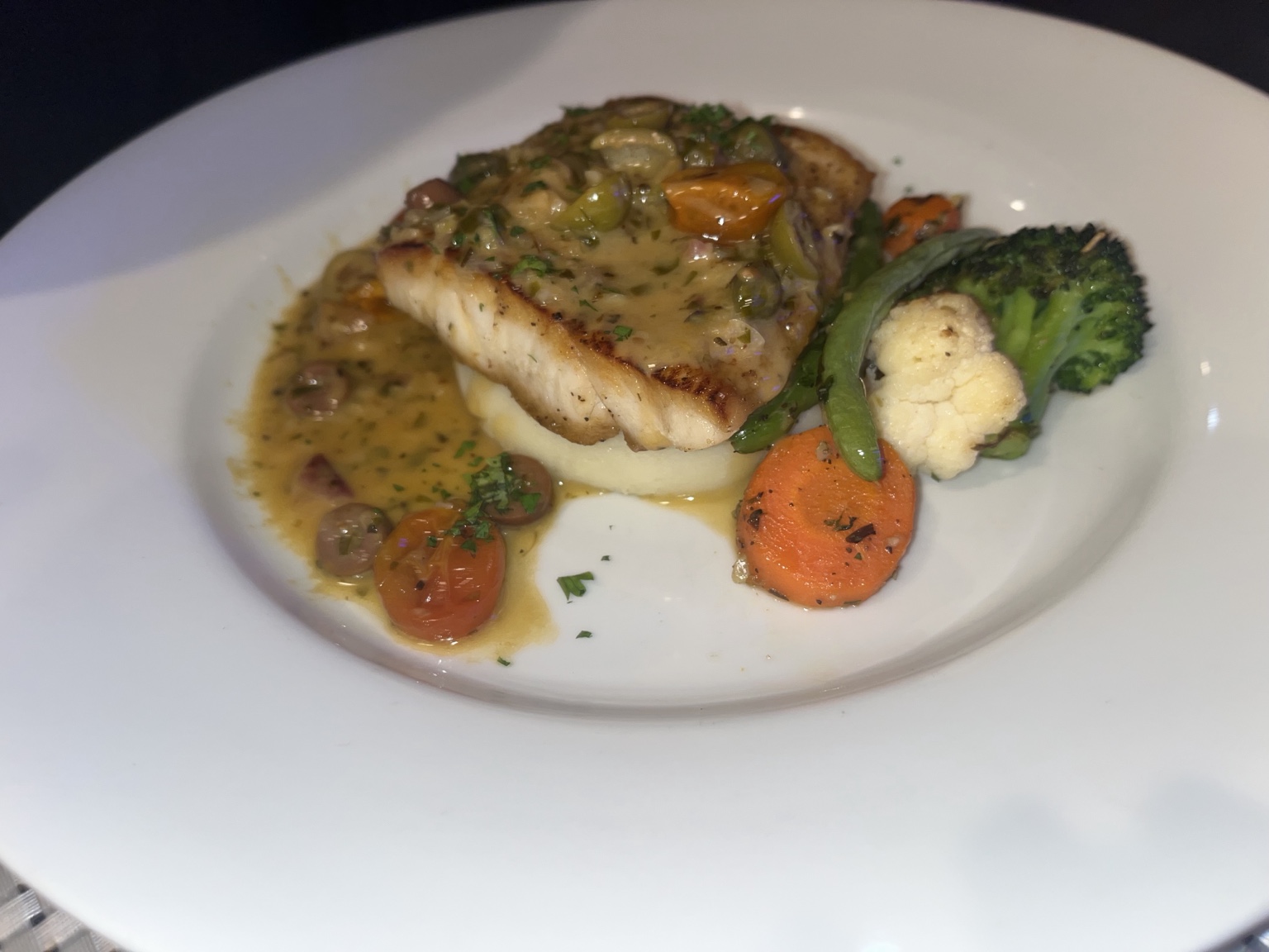 Seared fish over potato puree with olives, tomatoes and roasted vegetables