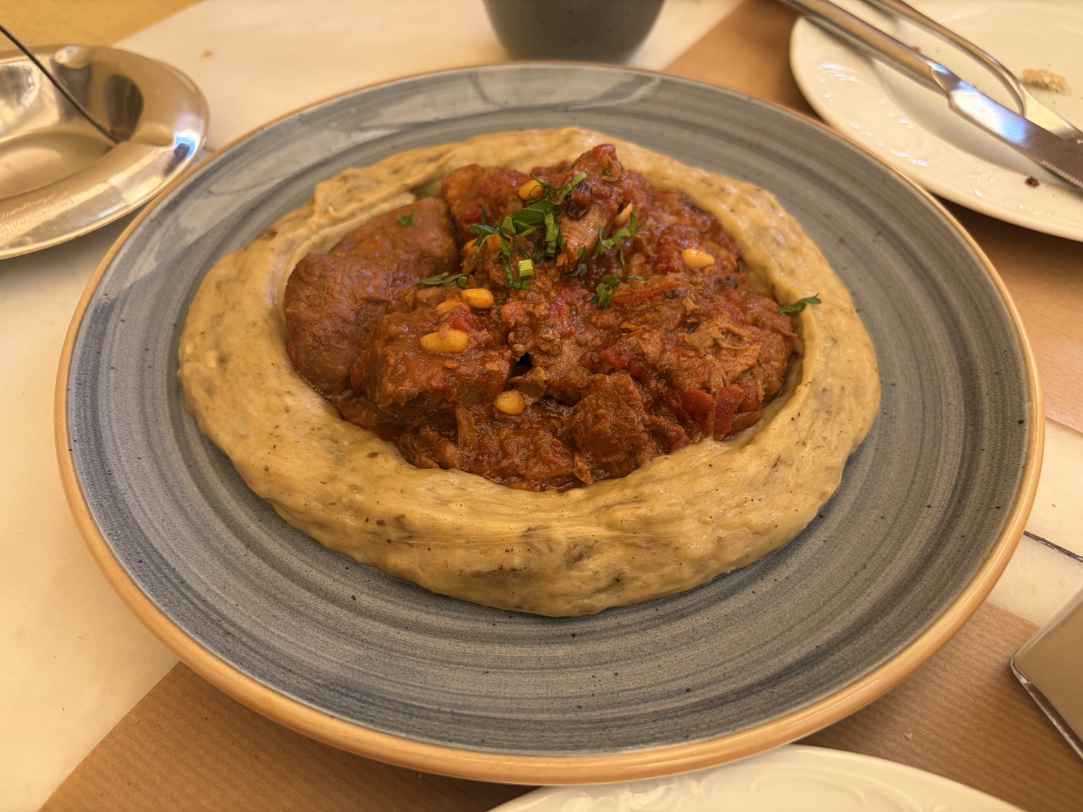 Braised meat in tomato sauce with creamy puree, pine nuts and herbs