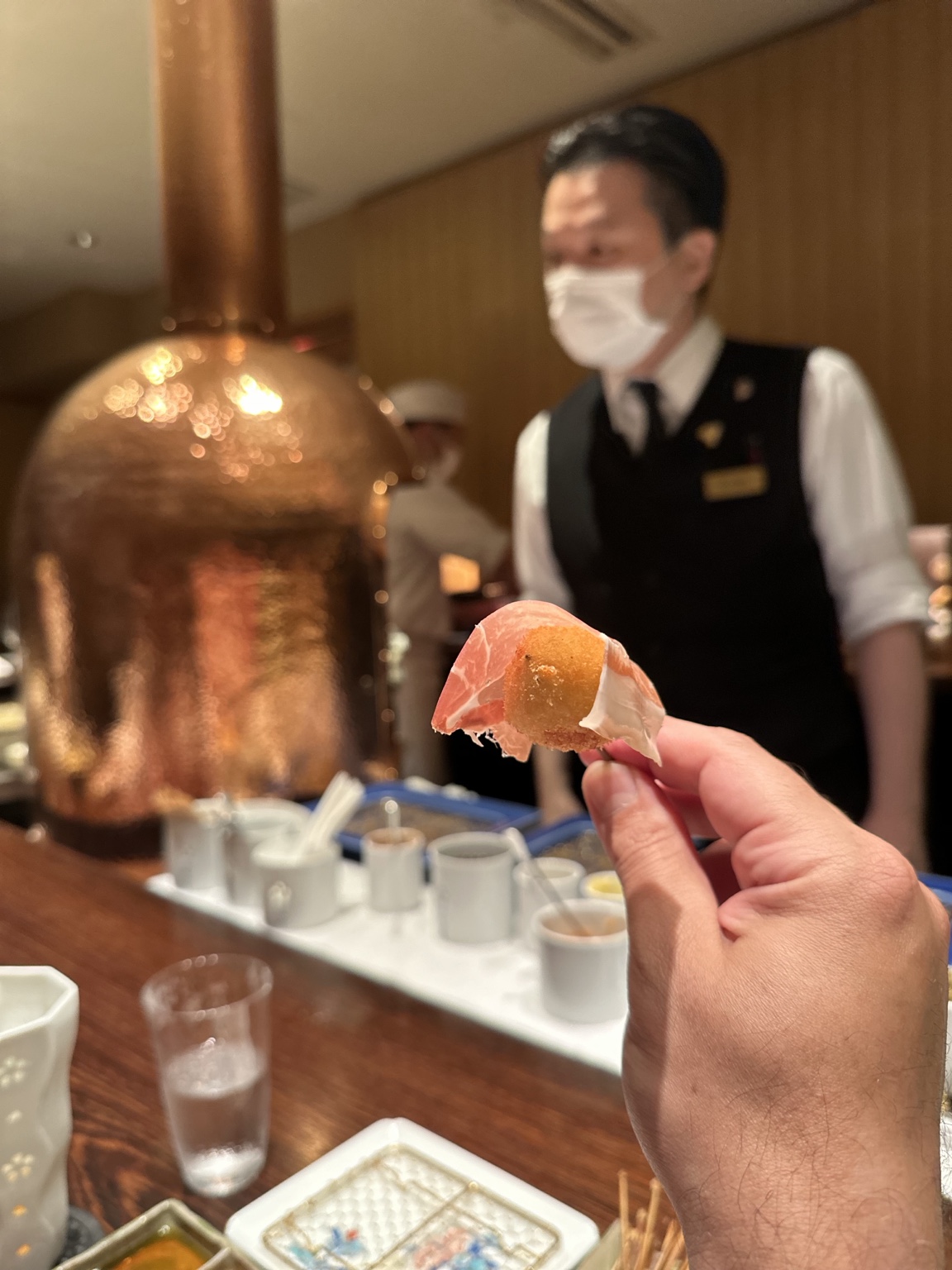 Hand holding a fried bite wrapped in cured ham