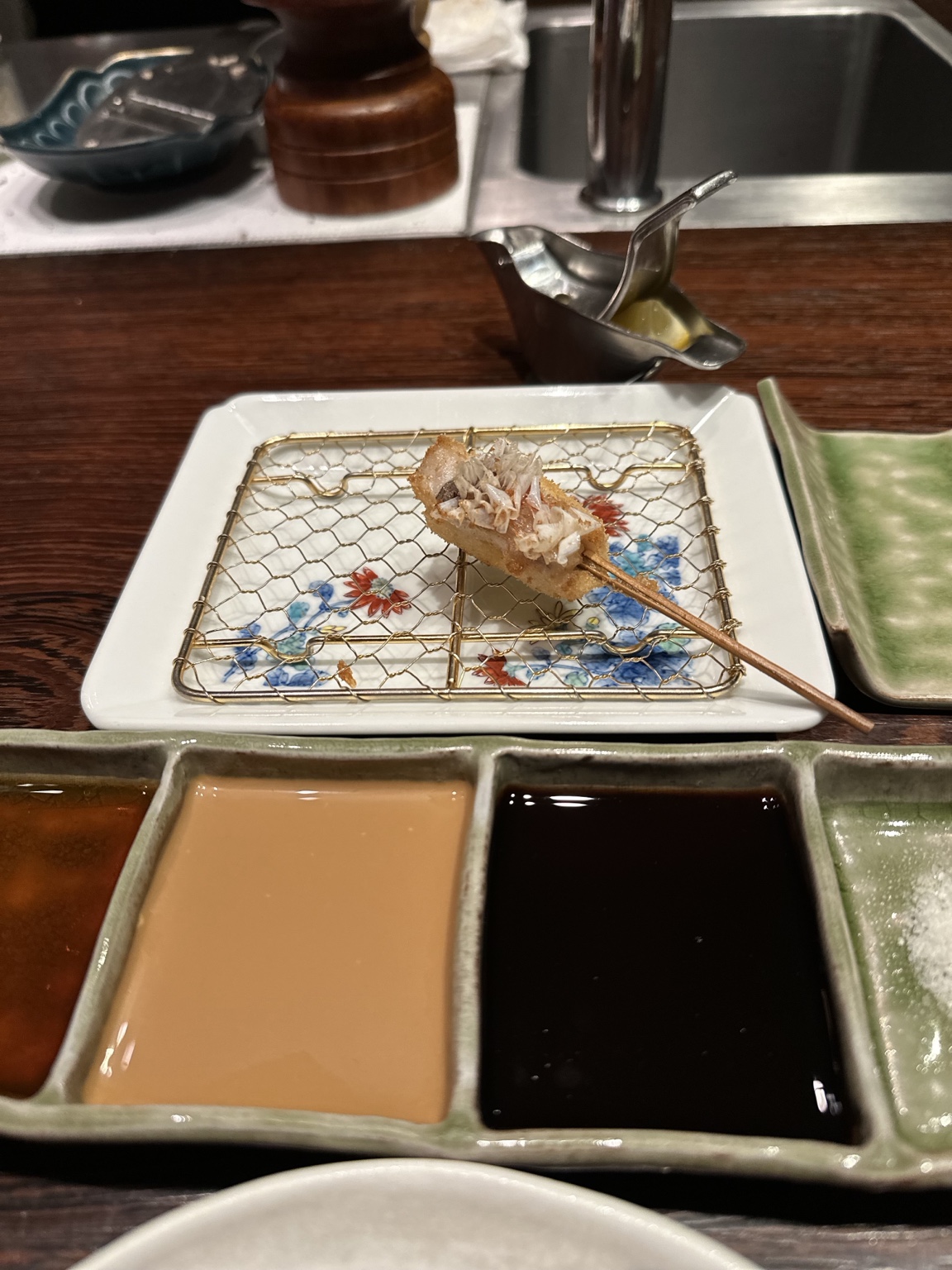 Crisp fried skewer topped with bonito flakes beside dipping sauces