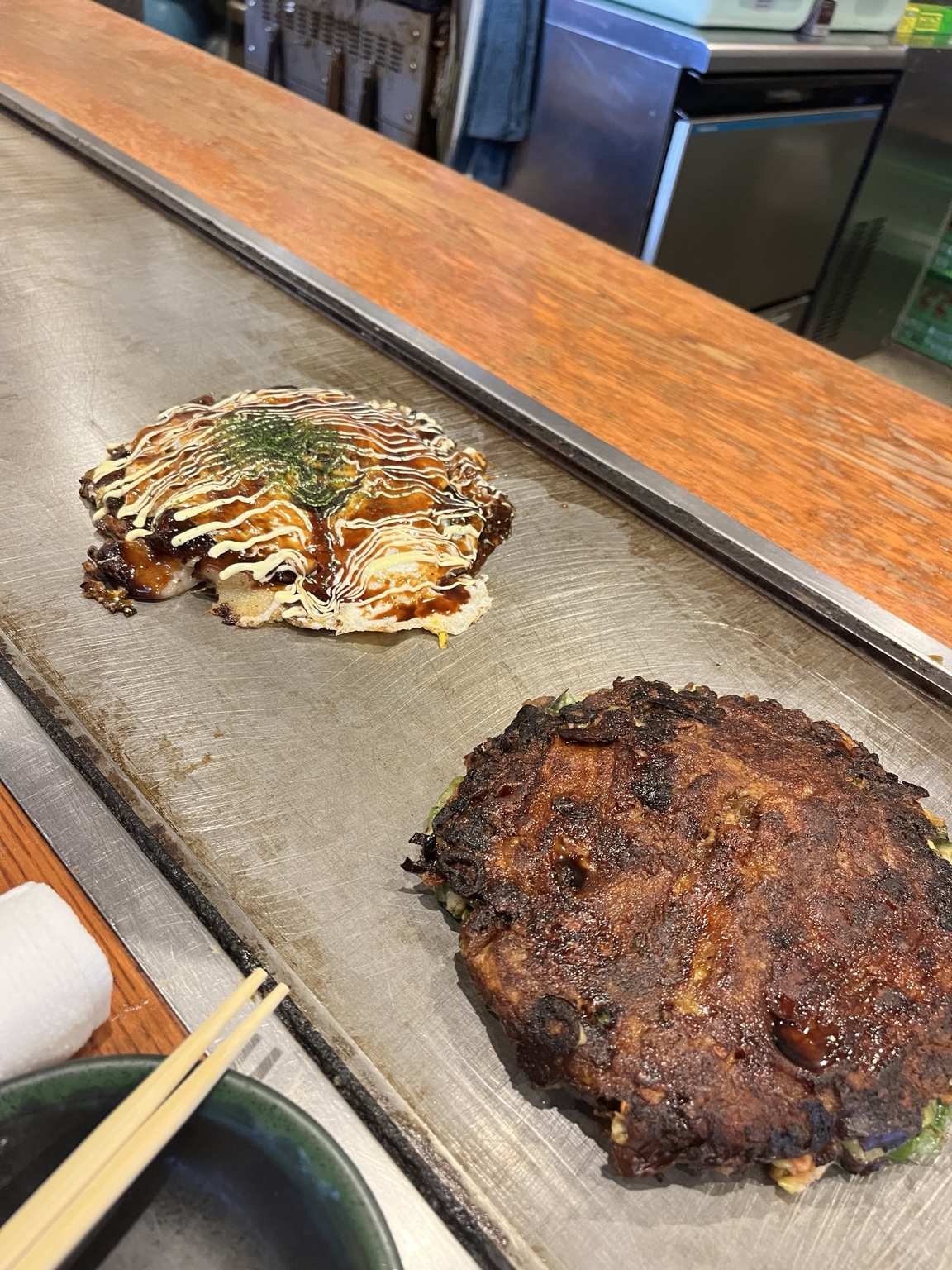 Two okonomiyaki savory pancakes cooking on a hot griddle