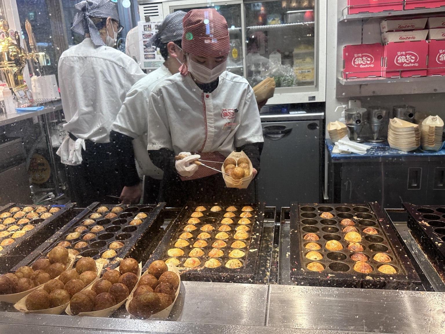 Cook preparing golden takoyaki balls on large griddles