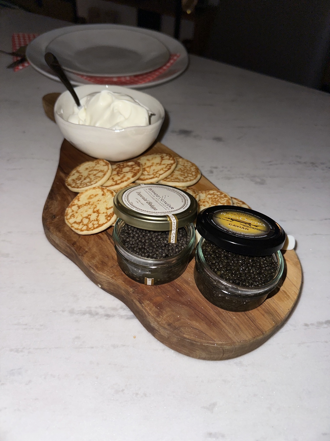Two jars of caviar with small pancakes and a bowl of cream